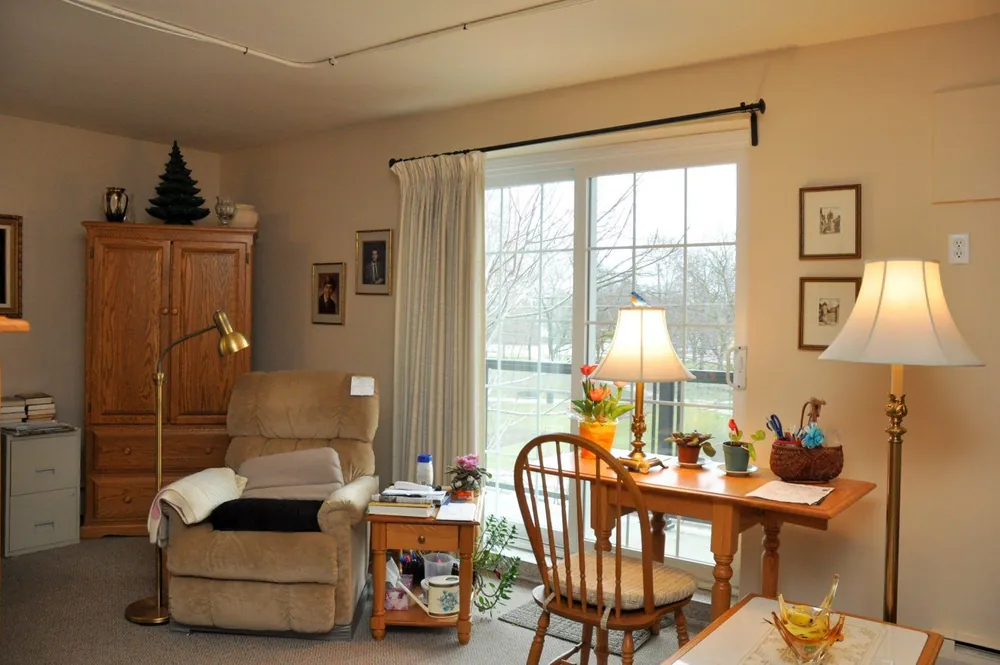 Resident suite sitting area with an armchair, writing desk and sliding door to a private balcony